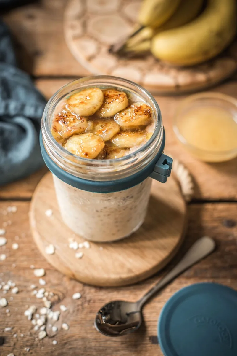 Close-up of creamy cinnamon-speckled banana oats topped with caramelised banana in the open glass jar