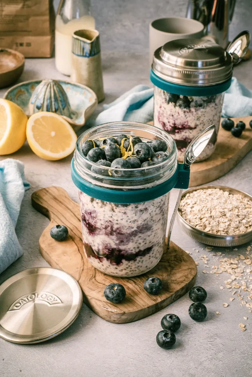 Blueberry and lemon overnight oats in an OATOLOGY glass jar topped with fresh blueberries and a curl of lemon zest