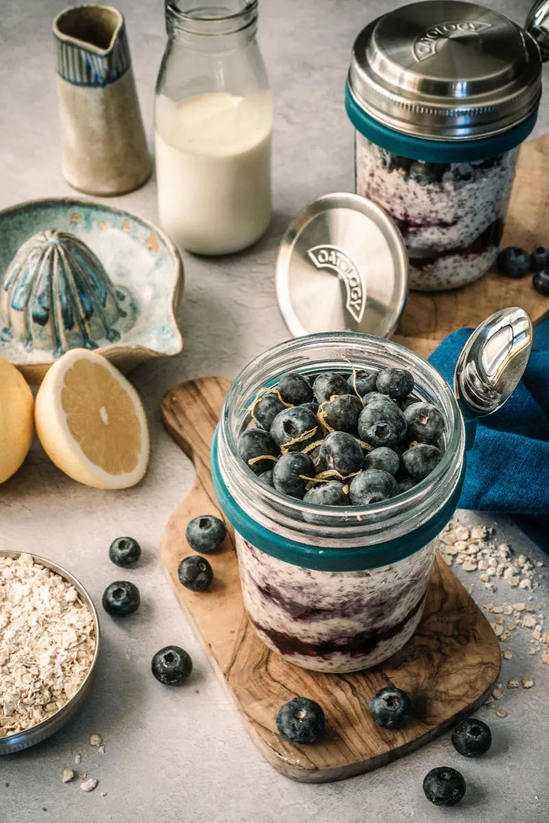 Close-up of creamy lemon oats speckled with chia and studded with blueberries in the open glass jar