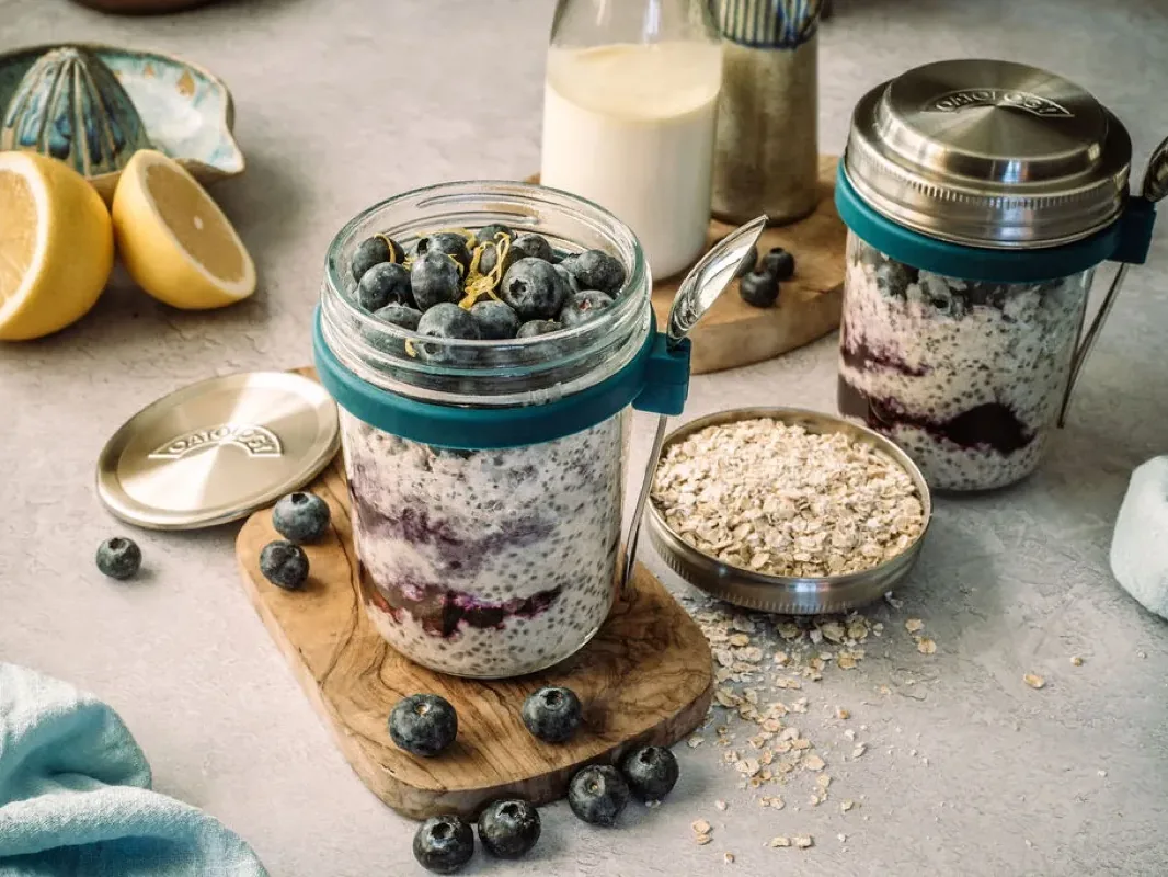 Sealed glass OATOLOGY jar of blueberry and lemon overnight oats made for the fridge, with the stainless steel lid alongside