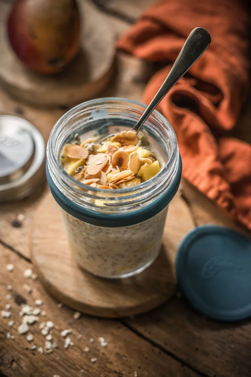 Close-up of chia-speckled coconut oats topped with mango and toasted almonds in the open glass jar